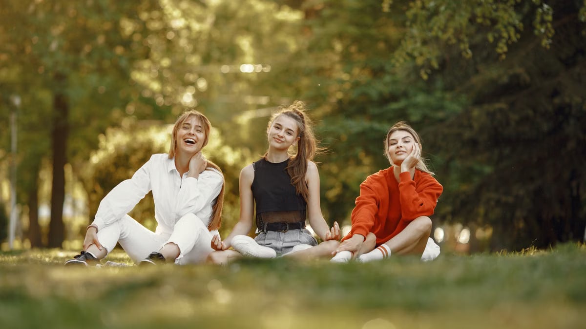 Three friends sitting on grass, enjoying a sunny outdoor day in the park.